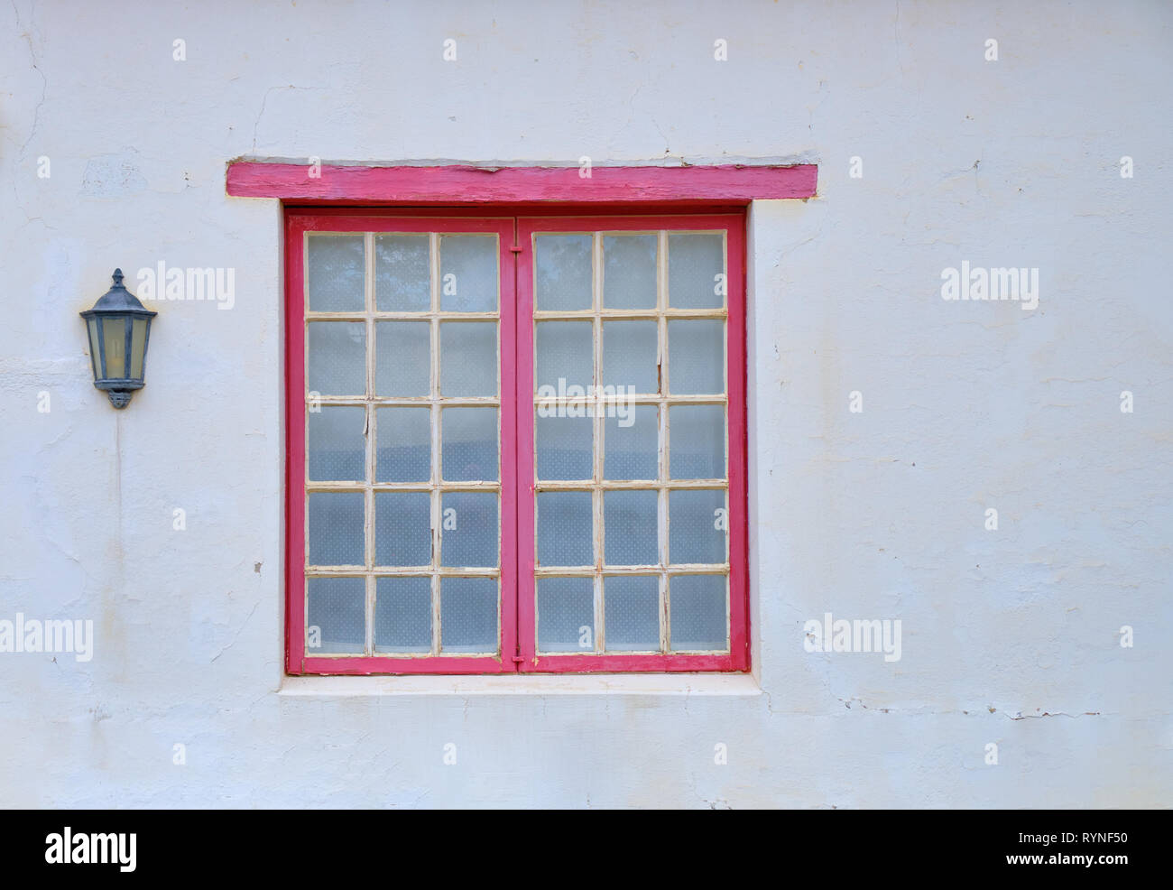 Minimalistische Erfassen eines einzelnen ländlichen Fenster auf einem weißen texturierte Wand. Fenster hat kleine Panels und einem roten Fensterrahmen. Es gibt ein Haus Licht Stockfoto