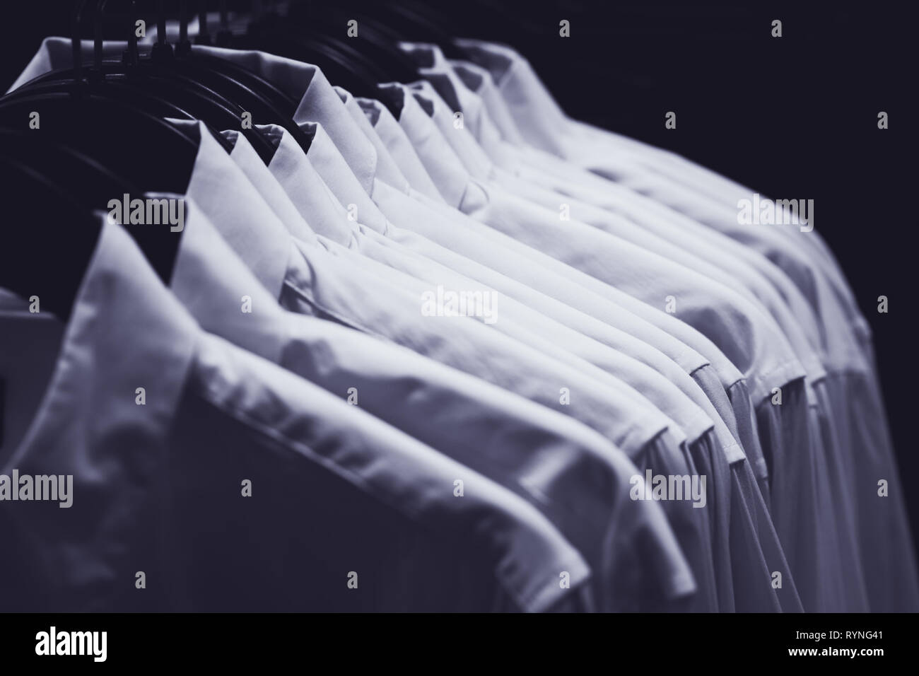 Reihe von weißen Hemden auf Kleiderbügeln hängen in der Finsternis der einen Kleiderschrank, getönt in Blau. Stockfoto