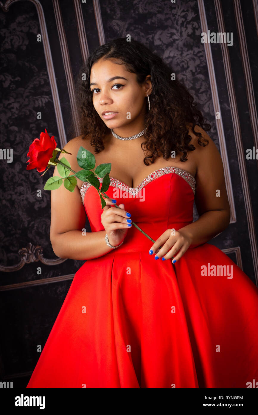 Eine schöne, biracial High School älteres Mädchen mit roten Kleid mit einer roten Rose Stockfoto