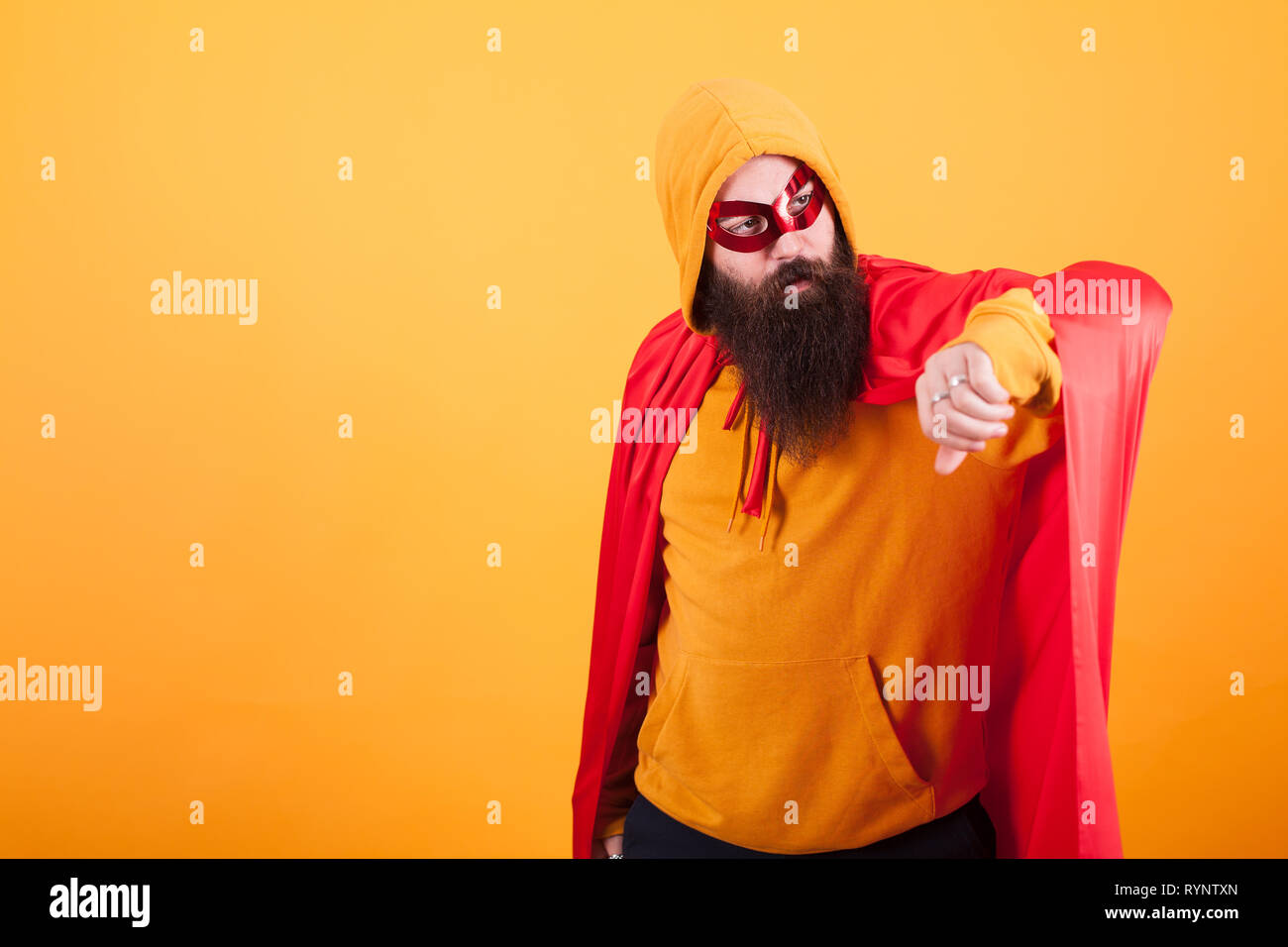 Hipster mit langen Bart in Superhelden Kostüm entfernt Blick auf gelben Hintergrund gekleidet. Gelbe hoodie. rote Maske. Tapferer Mann. Stockfoto