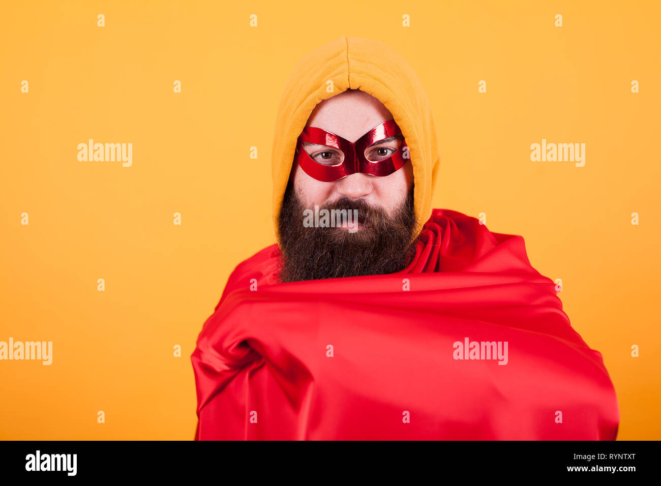 Bärtige Superhelden mit rote Maske mit seinem roten Cape zeigt auf gelben Hintergrund. Stattliche Superhelden. Stockfoto