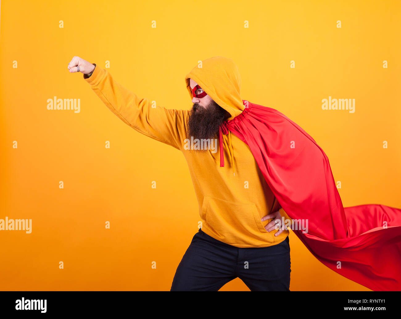 Superhelden mit rotem Umhang und Maske weg fliegen im Studio über gelben Hintergrund., mutiger Mann. Stattlich. Stockfoto
