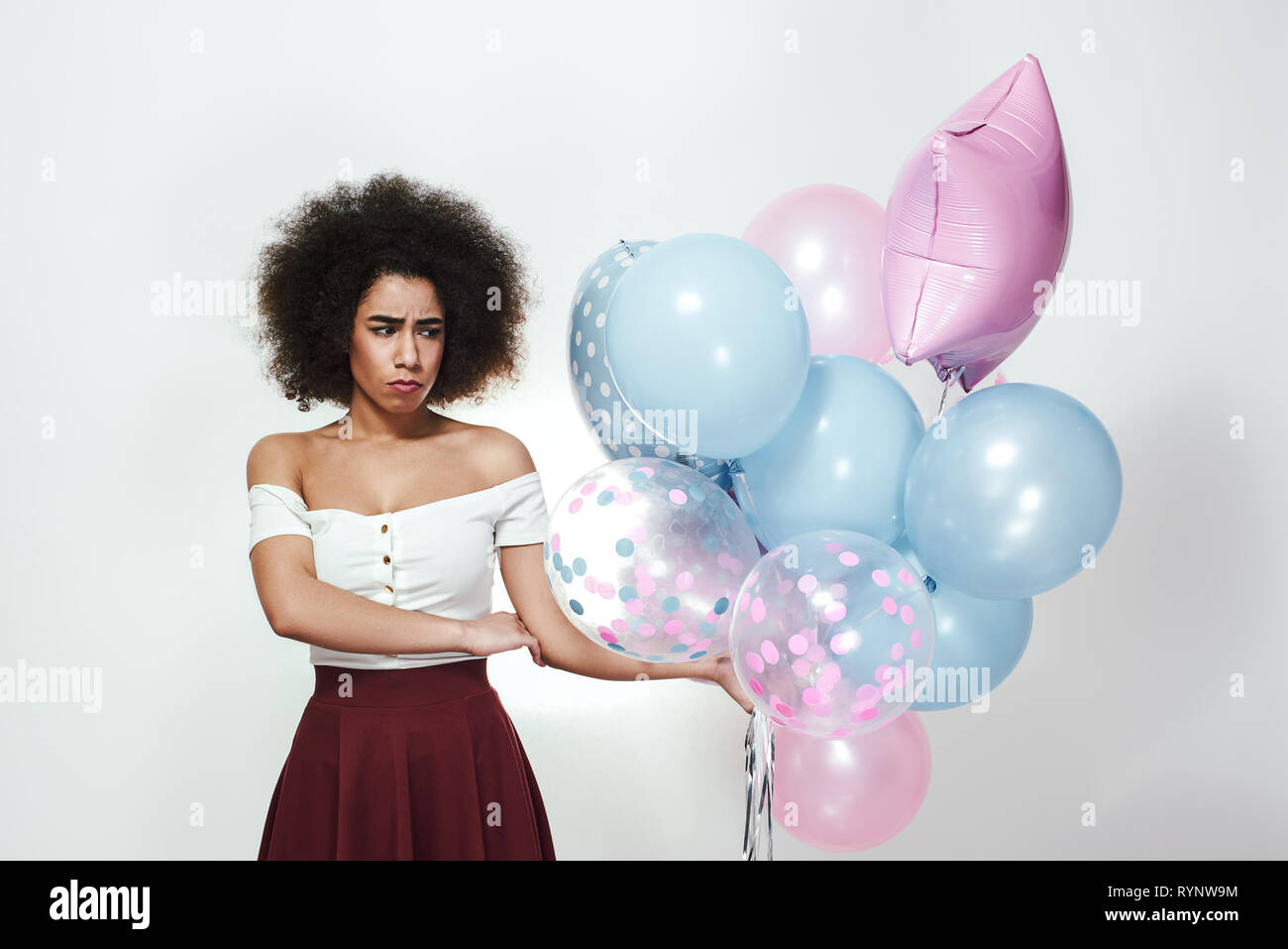 Keine macht mehr Spaß. Traurig und langweilig junge afro-amerikanische Frau mit einem Bündel von bunten Luftballons und ein Gesicht, während gegen grauen Hintergrund stehen. Negative Emotionen. Stockfoto