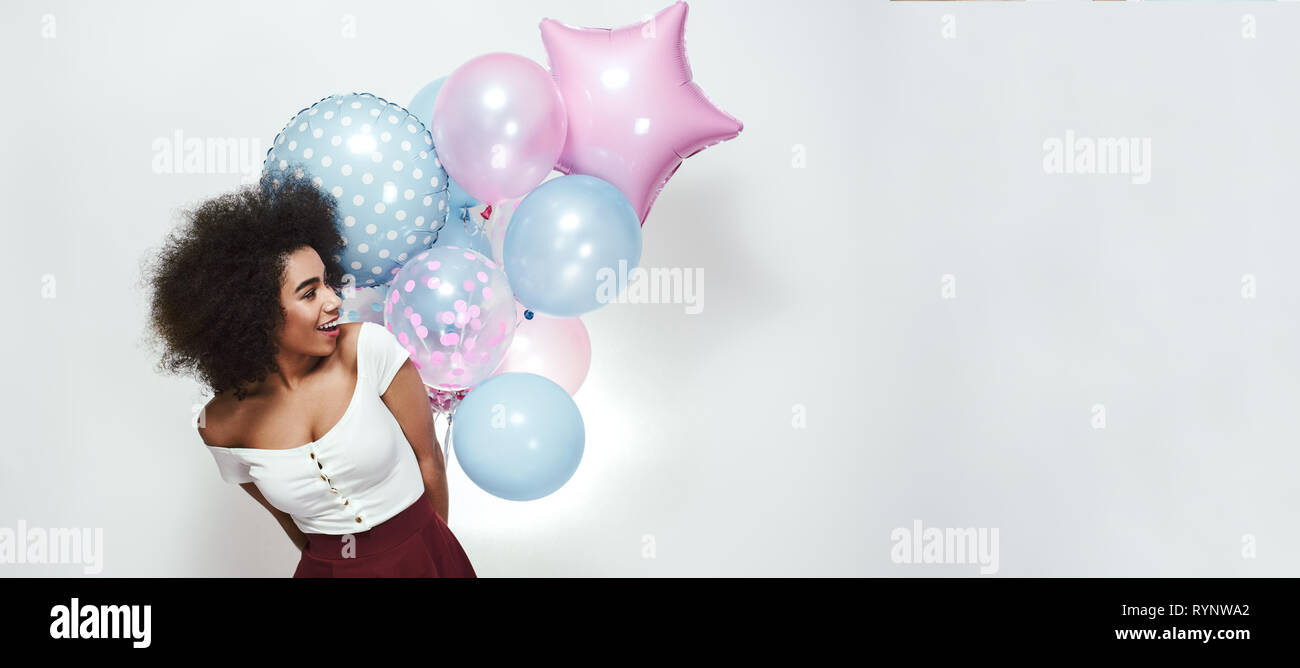 Schöne Erinnerungen! Fröhlich und hübsche junge afro-amerikanische Frau mit lockigem Haar hält Bündel von bunten Luftballons und weg schauen. Web Banner. Party Konzept. 16 x 9-Format Stockfoto