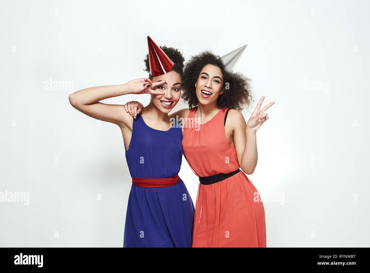 Party Feier. Porträt von zwei positive und junge afro-amerikanische Frauen in schönen Abend Kleider und Hüte zeigen Friedenszeichen und Lachen. Geburtstag Konzept. Glückliche Momente Stockfoto