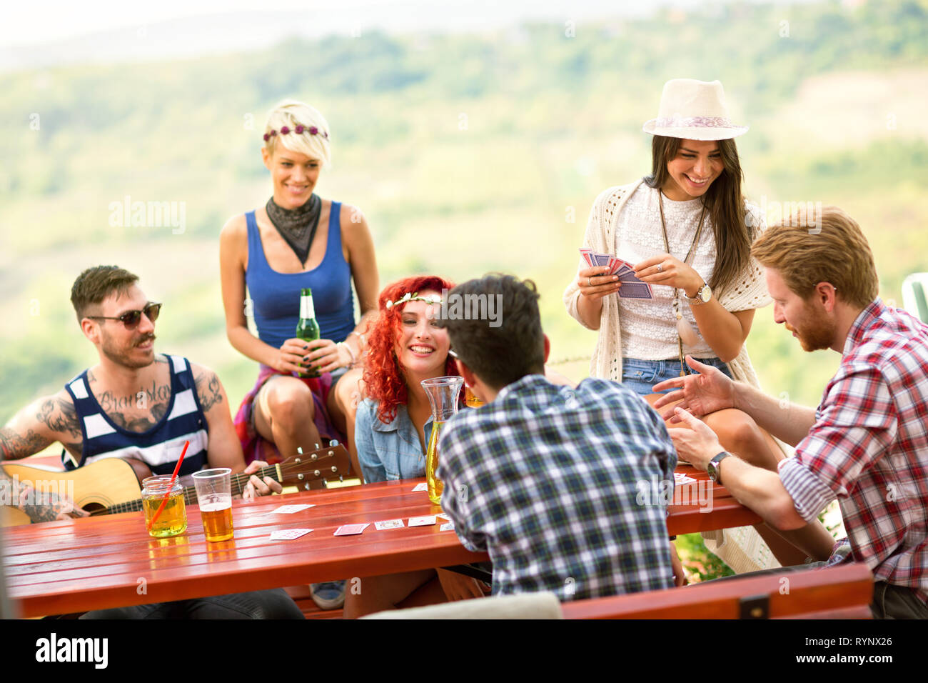 Fröhliche Gruppe von jungen Freunden Karten spielen, Gitarre und Getränke im Freien im Sommer Stockfoto