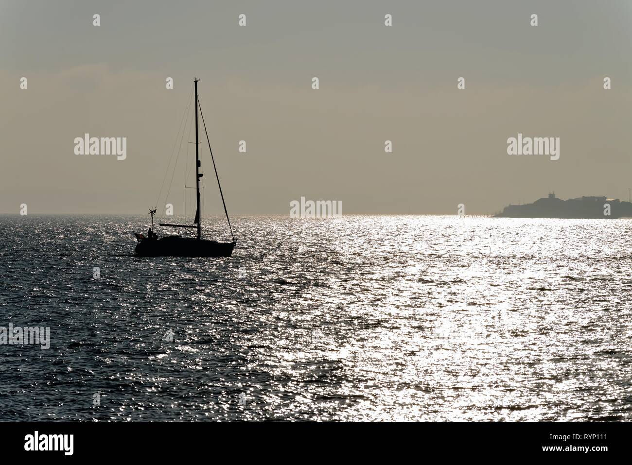 Silhouette einer Yacht segeln auf den Solent in Portsmouth Hampshire, gegen die Reflexion von Sonnenlicht auf dem Meer, England Großbritannien Stockfoto