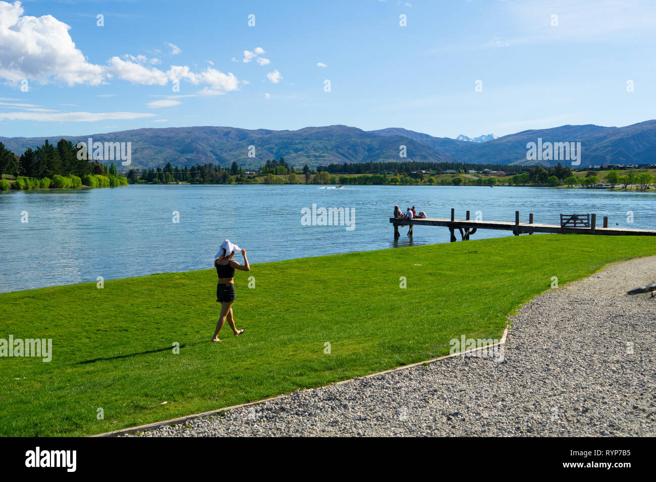 CROMWELL NEUSEELAND - 21. Oktober 2019; Lake Dunstan Szene mit junge Frau wlking entlang dem Rand und Gruppe junge Leute zusammen sitzen am Ende der j Stockfoto