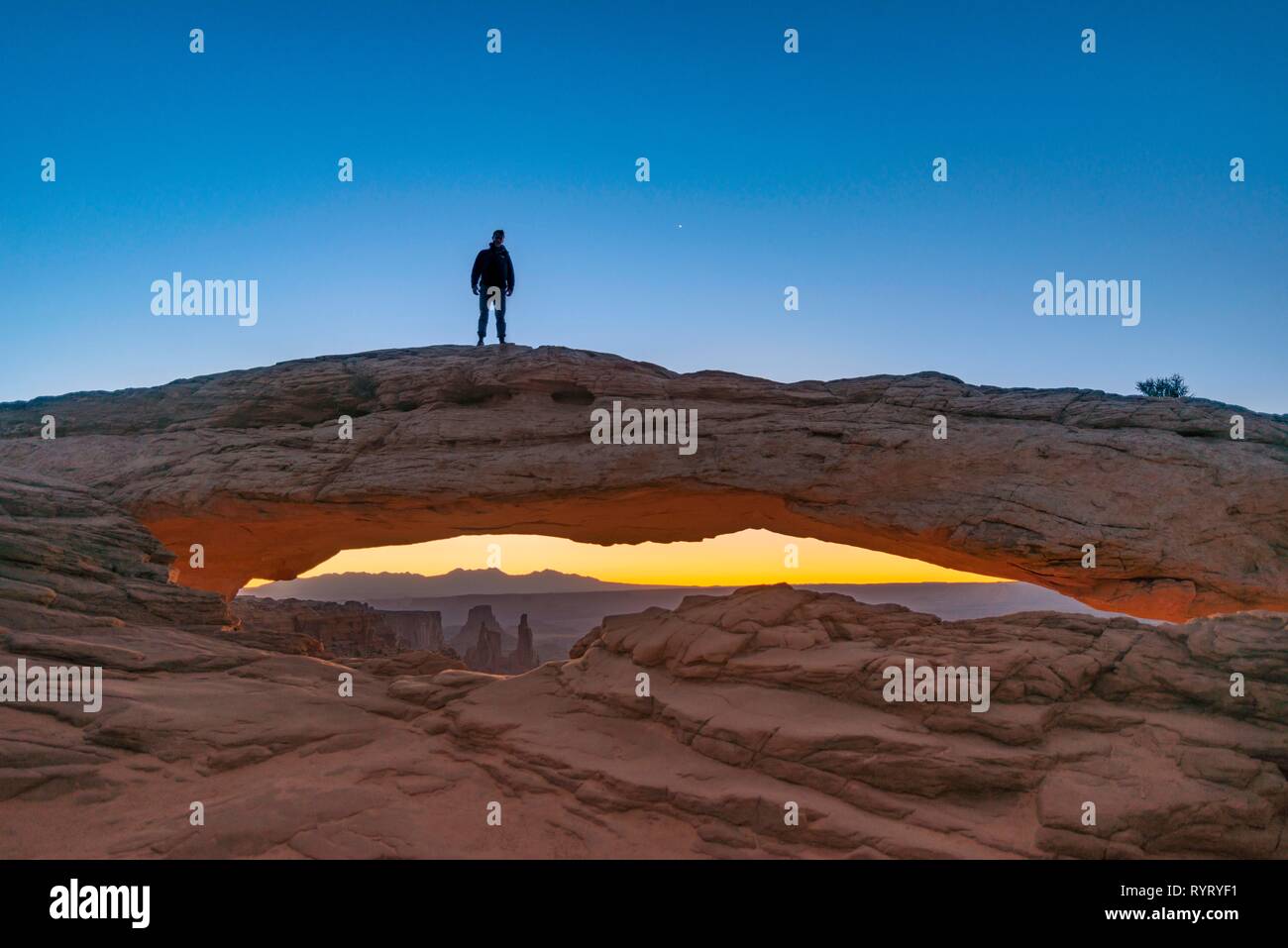 Junger Mann steht auf Rock Arch, Mesa Arch, Sunrise, Grand View Point Road, Insel im Himmel, Canyonlands National Park, Moab Stockfoto