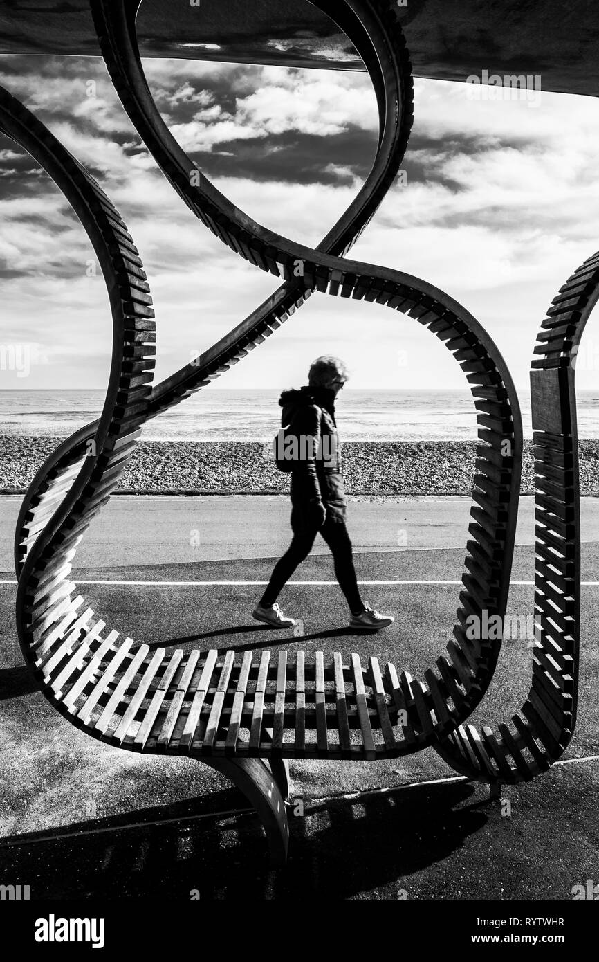 Frau Spaziergänge entlang der Strandpromenade und durch's Studio weben lange Bank Projekt eingerahmt. Eine funktionale Bank, Platz für bis zu 300 Personen. Stockfoto