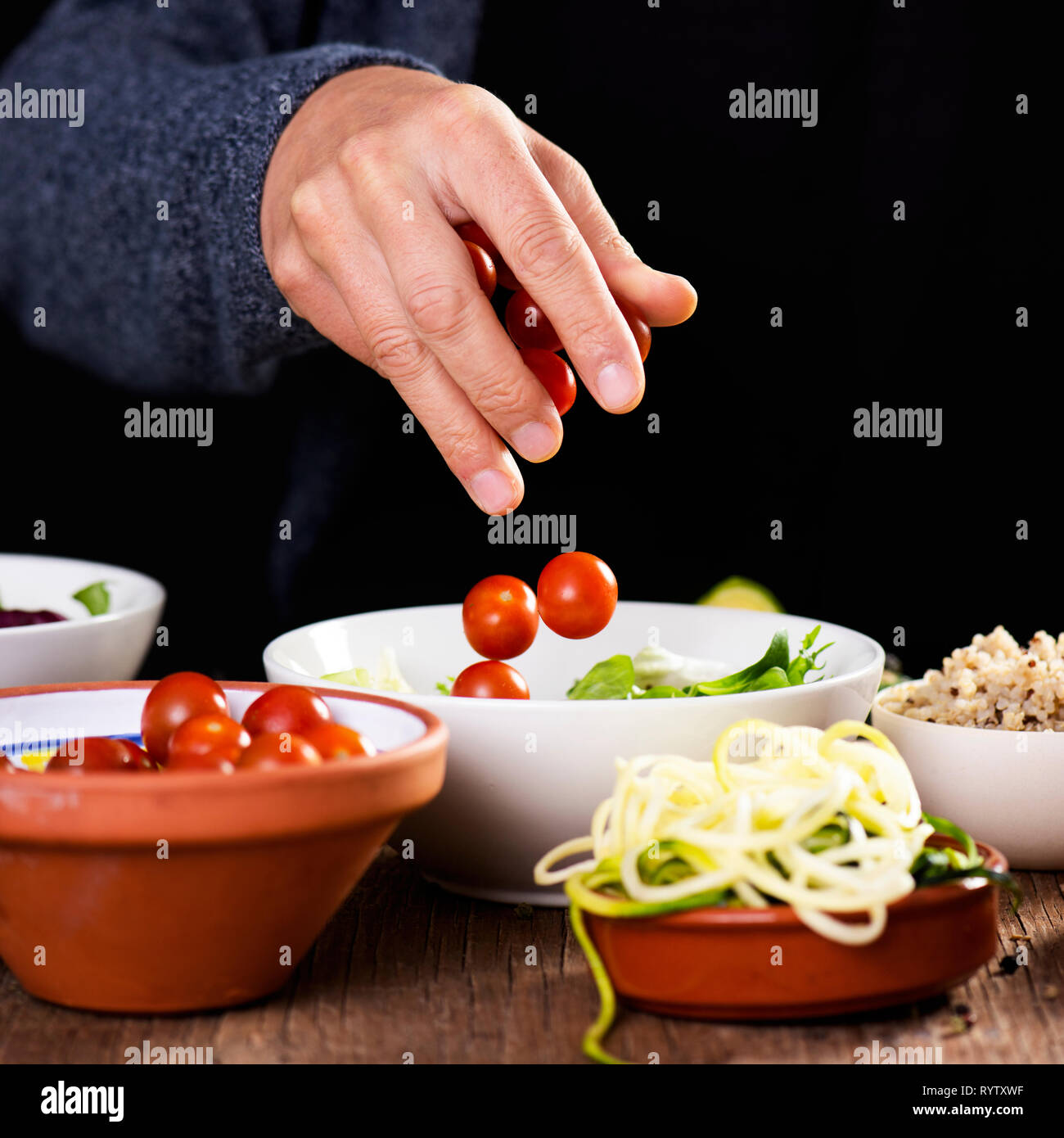 Nahaufnahme eines jungen kaukasischen Mann Vorbereitung eines Buddha Schüssel Salat, mit unterschiedlichen Zutaten, wie Salat, cornsalad, Quinoa, Zucchini Spaghetti oder Stockfoto