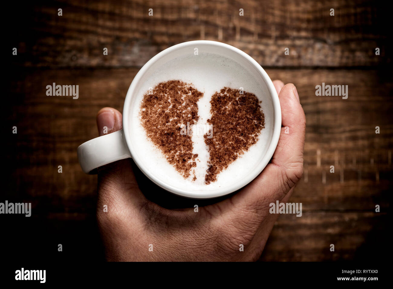 Hohe Betrachtungswinkel von einem kaukasischen Mann hält eine weiße Keramik Tasse Cappuccino, mit einem gebrochenen Herzen mit Kakaopulver auf dem Milchschaum gezeichnet, auf einem Tropfen Stockfoto