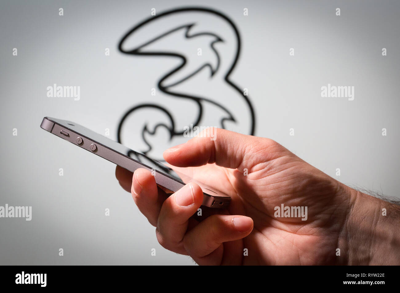 Ein Mann mit einem Handy vor den drei Mobile Network Logo Stockfoto