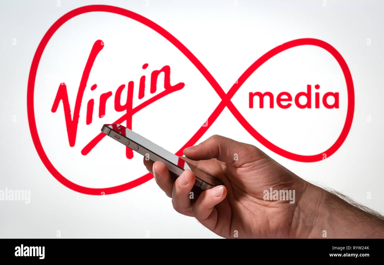 Ein Mann mit einem Handy vor einem Virgin Media Logo Stockfoto