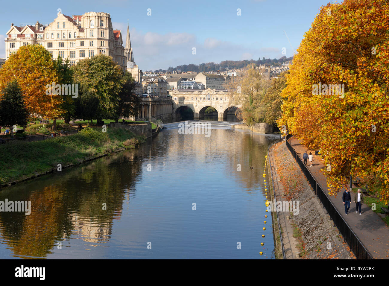 Badewanne, Großbritannien - 20 Oktober, 2018: die Menschen zu Fuß von Pulteney Wehr und Pulteney Bridge durch lebhaften herbstlichen Bäume am Fluss Avon in Bath, UK umgeben. Stockfoto