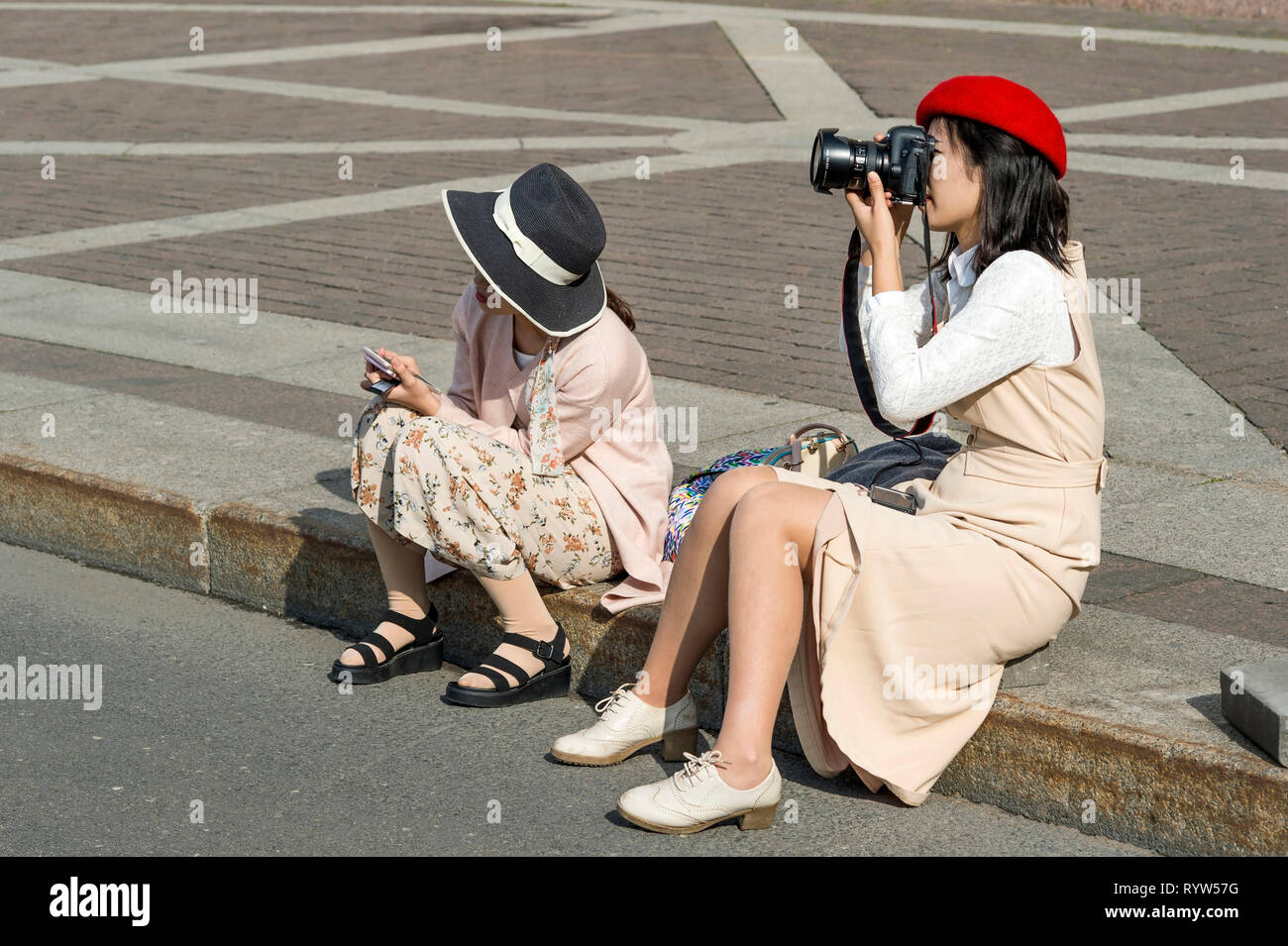 Eine junge Frau und ein Mädchen der Östlichen Aussehen in hellen Pastelltönen Kleidung und Hüte, sitzt auf dem Bürgersteig, Bilder der Sehenswürdigkeiten der Palace s nehmen Stockfoto