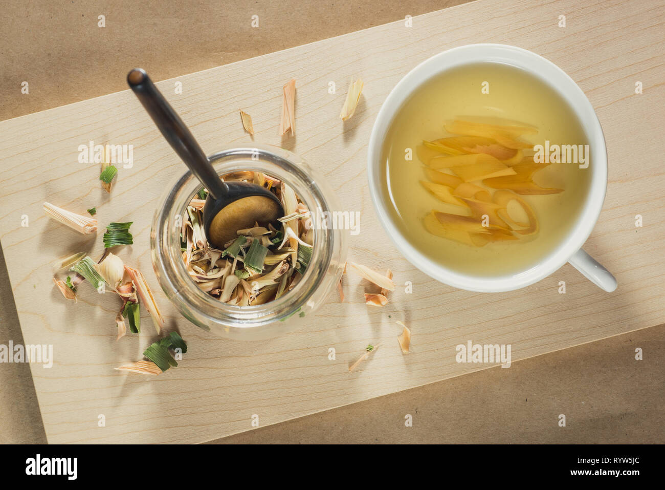 Tasse Zitronengras Tee und ein Glas Glas mit getrockneten Blätter von zitronengras. Holz und Papier Hintergrund. Ansicht von oben. Stockfoto
