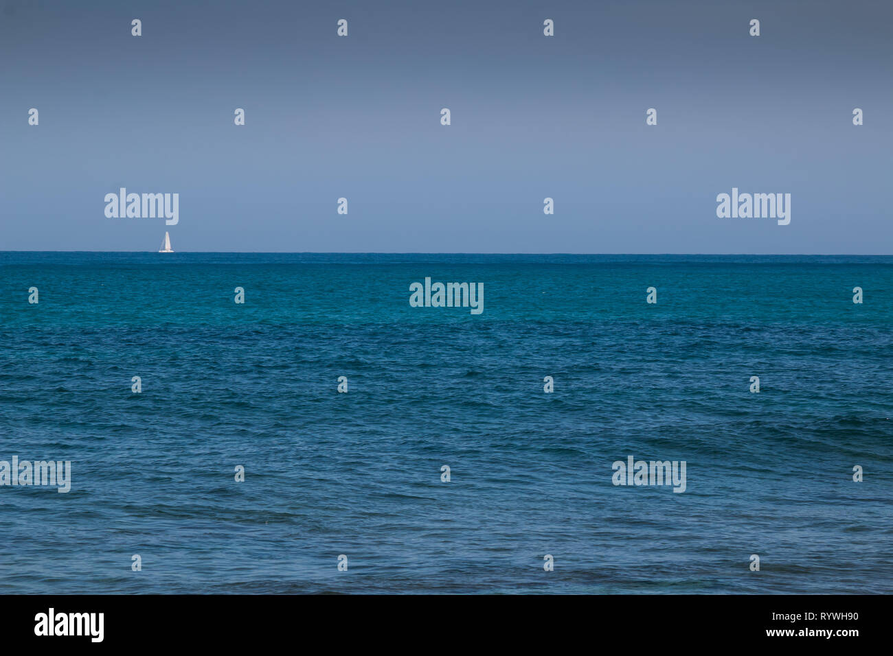 Die blauen und grünen Farben der Wasser des Mittelmeers, mit kleinen Wellen. Weißes Segelboot am Horizont. Blue Sky. Gouves, Kreta, Griechenland. Stockfoto