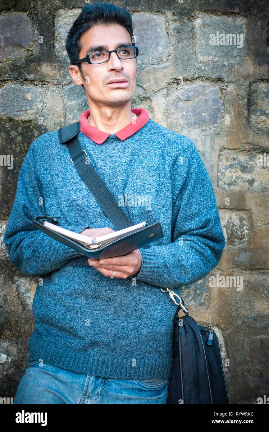 Asiatischen, Indischen serene junger Erwachsener Geschäftsmann holding Business Planner und denken, wenn Sie sich an betrachten. Er steht mit der Unterstützung von Wall Stockfoto