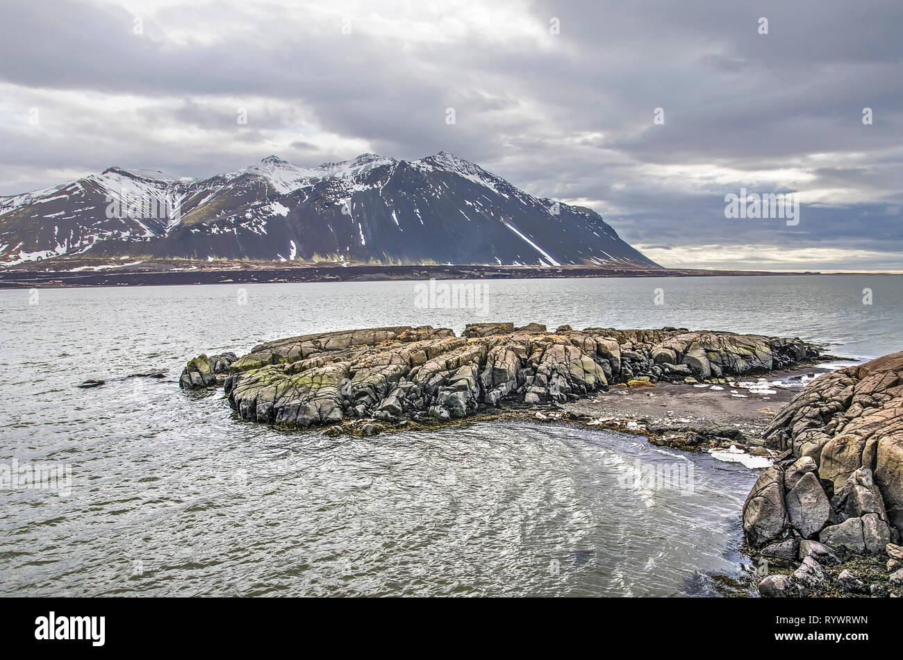 Niedrige Felsformation an der Küste in der Nähe von Borgarnes, Island, mit Blick auf den Fjord, die schneebedeckten Berge und den Ozean Stockfoto