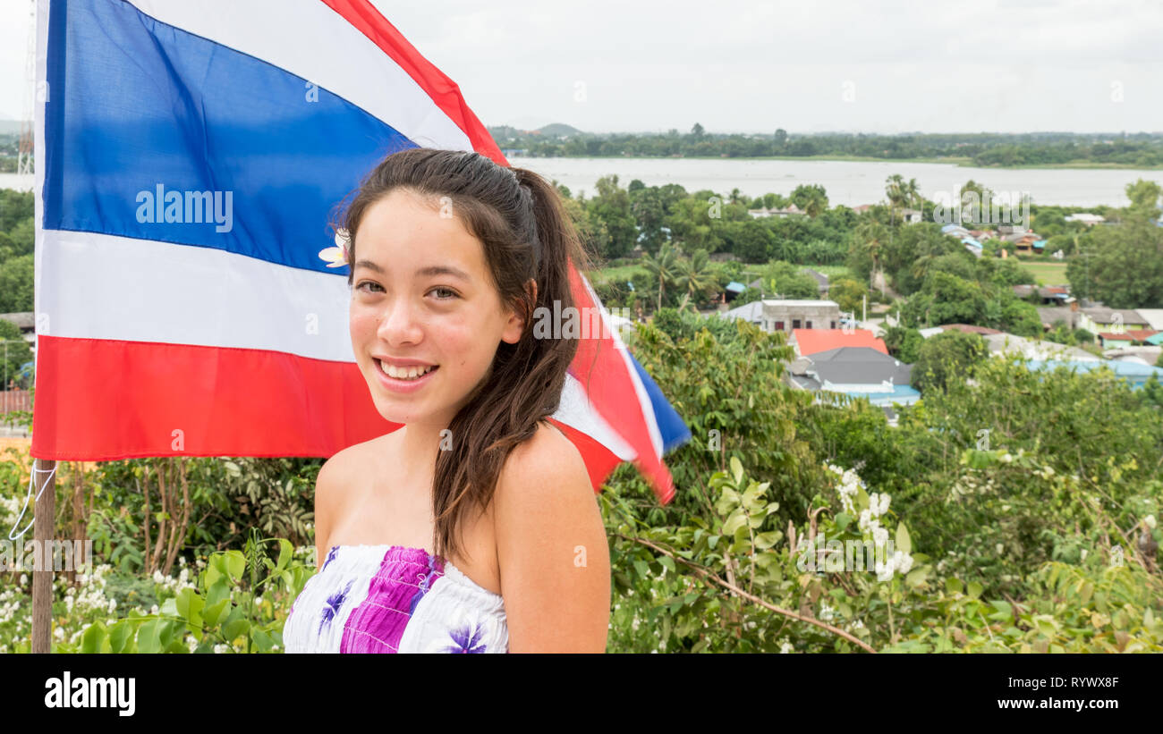 Lächelnd jugendlich stand vor der Thailändischen Fahne mit der Stadt im Hintergrund Stockfoto