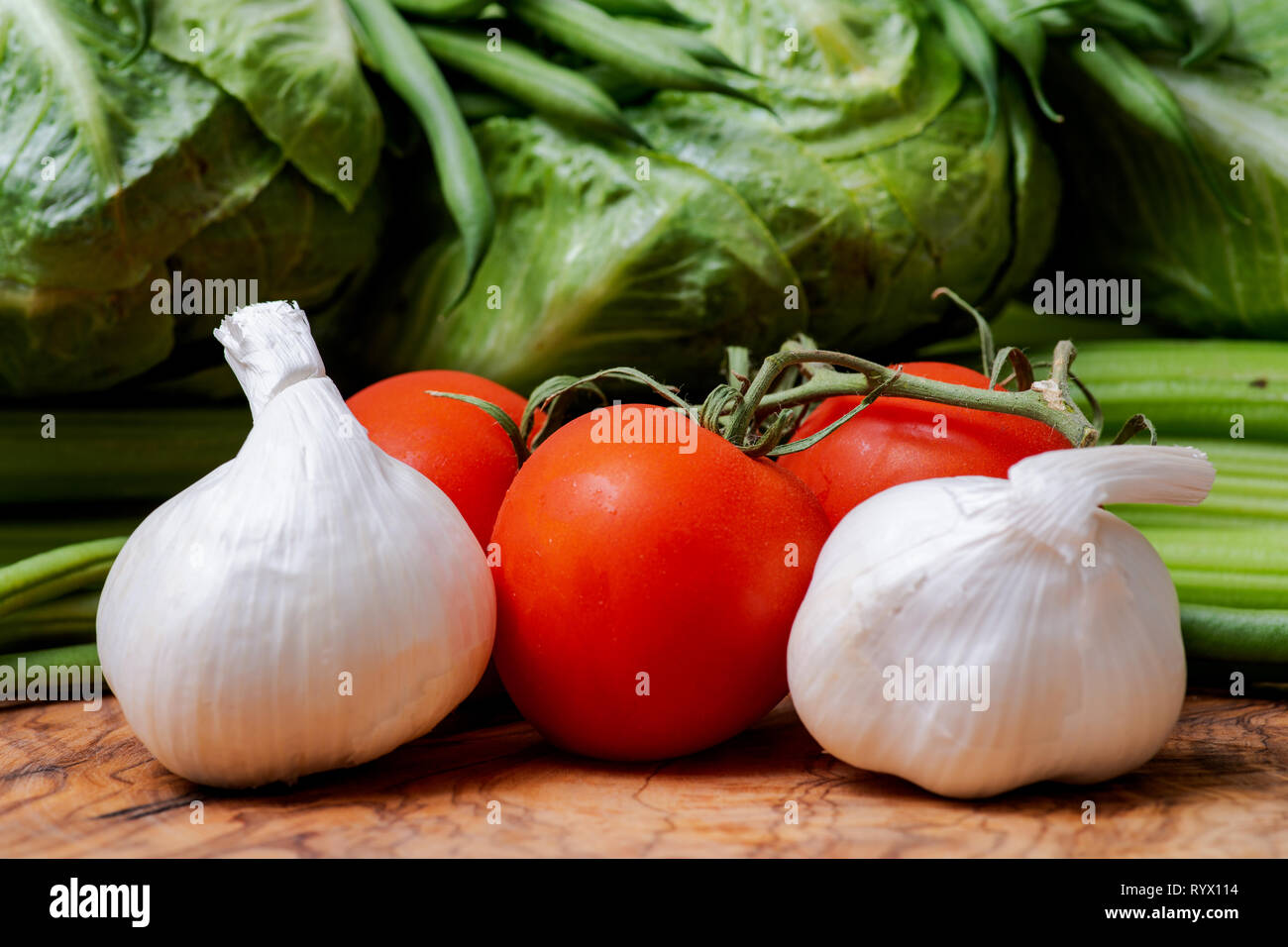 Organische Rohe ganze Knoblauch Zwiebeln und rote Tomaten auf der Rebe auf natürliche Olivenholz angeordnet. Allium Sativum. Solanum Lycopersicum. Stockfoto