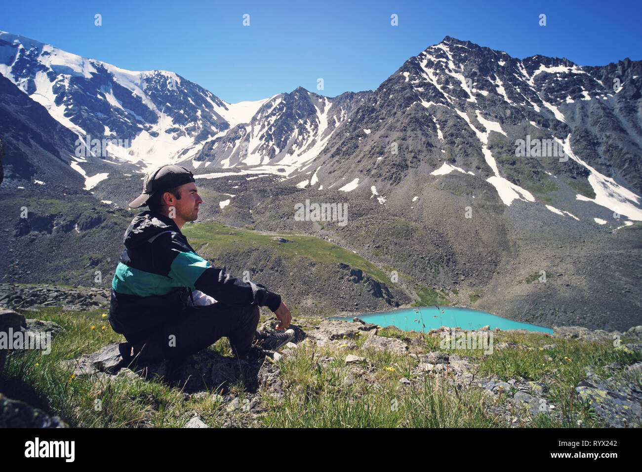 Junge Mann in Schwarz Sportswear sitzt auf der Klippe und suchen Tal unten, Misty. Schönen Hintergrund Landschaft mit hohen Bergen mit s Stockfoto
