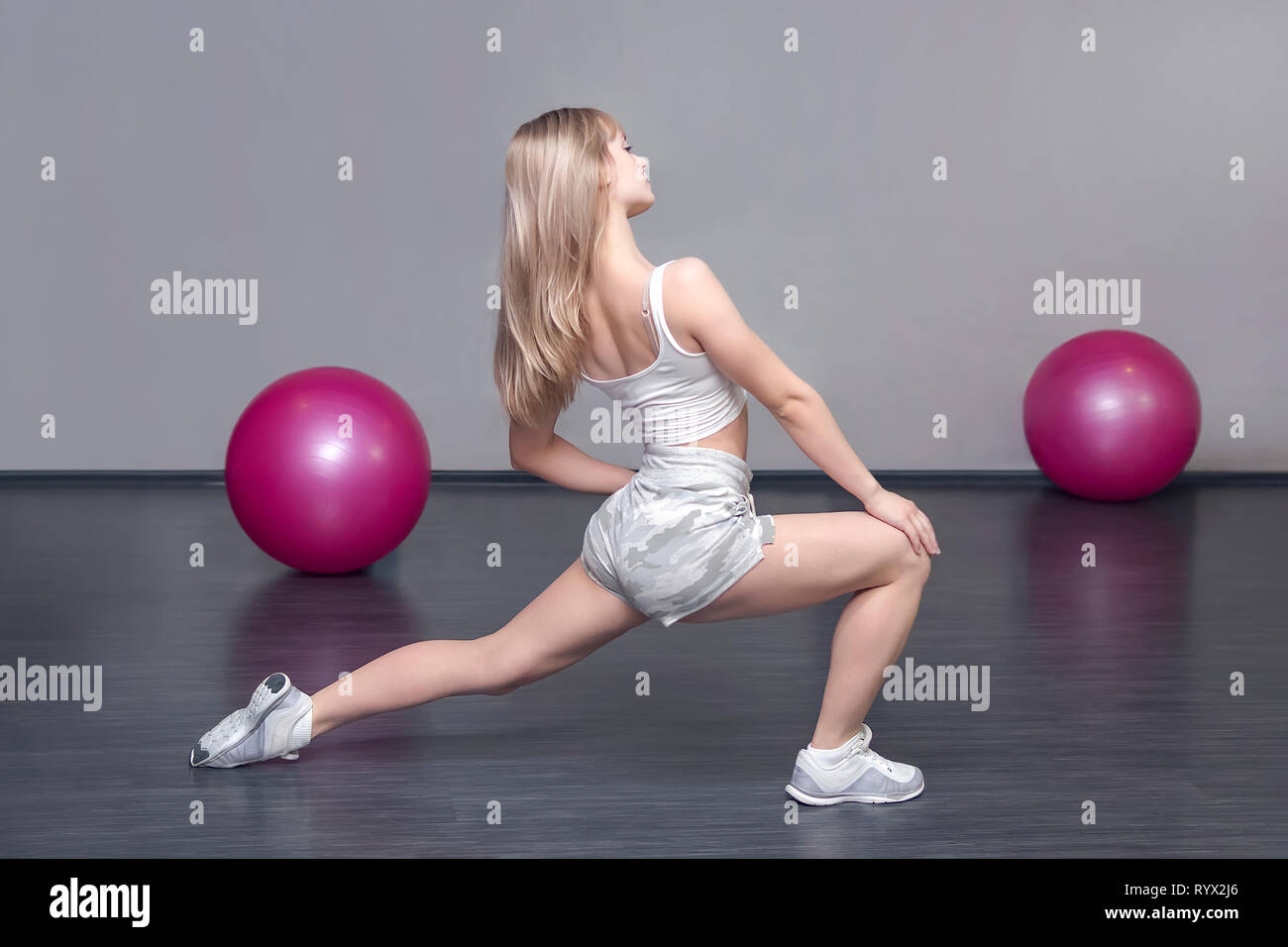 Blond Sportlich kaukasischen Lady ist in der Turnhalle während des Trainings. Übungen, die Muskeln auf die Beine zu strecken. Warm-up vor dem Training. Women's Fitness. Stockfoto