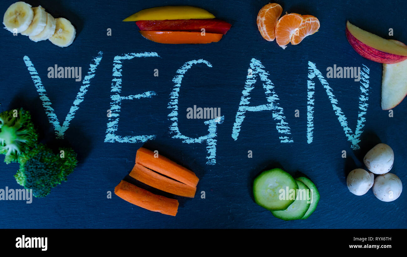 Das Wort vegan in Kreide auf Schiefer, umgeben von Obst und Gemüse geschrieben. Vegane Küche. Veganuary. Werkbasiert Stockfoto