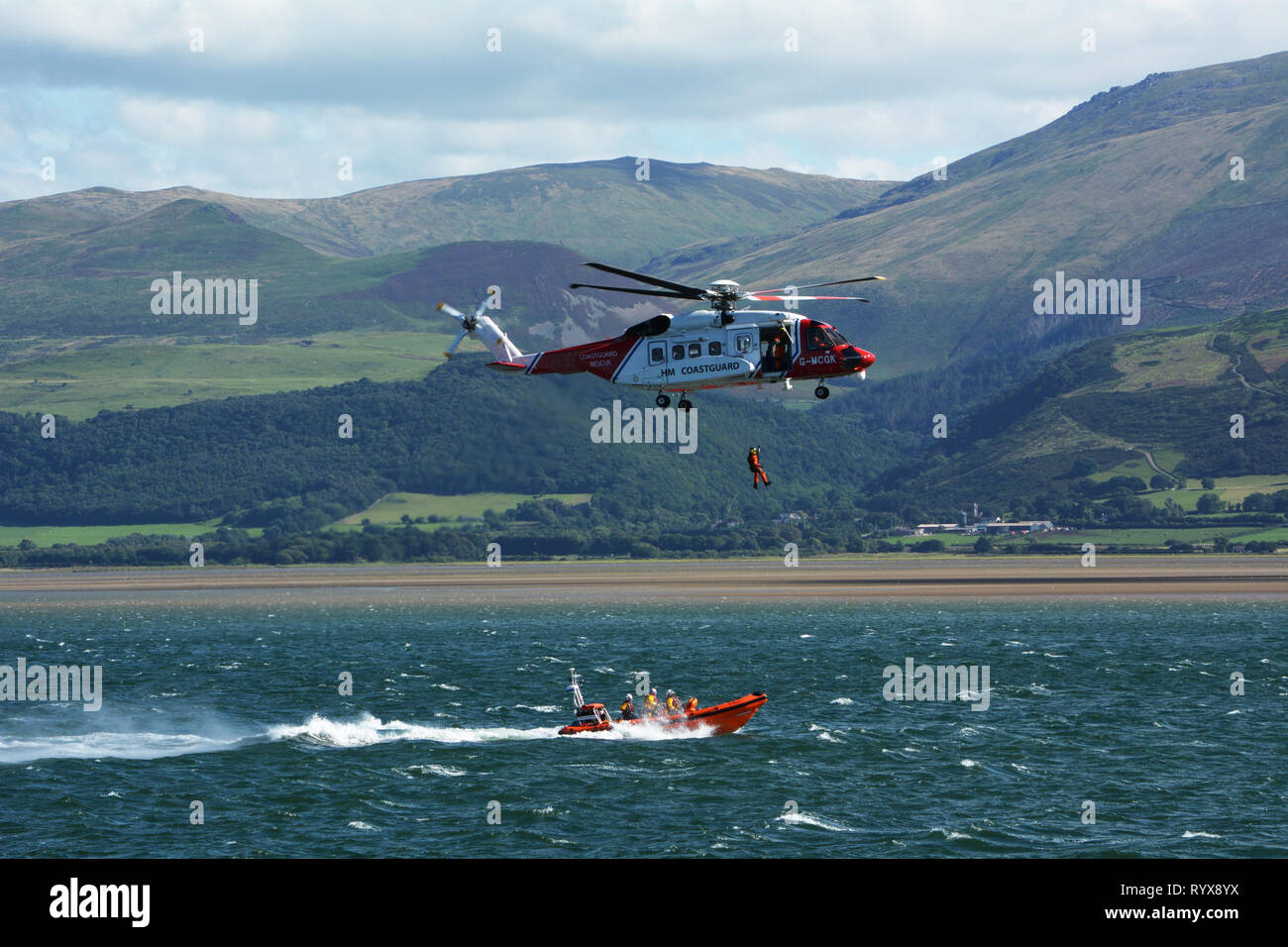 HM Küstenwache Hubschrauber und Beaumaris Rettungsboot Praxis übertragen Einer gerettet Person auf der Menaistraße mit Snowdonia Berge im Hintergrund Stockfoto