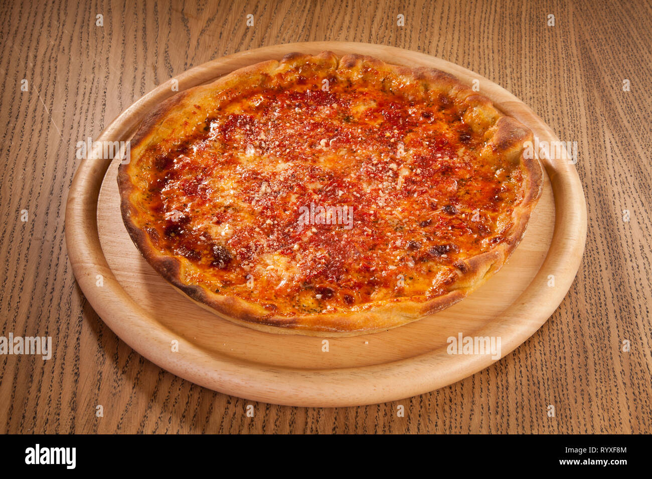 Pizza mit Käse heiß serviert und lecker auf Holzplatte auf Tisch. Schnelle und kostengünstige Mahlzeit Stockfoto