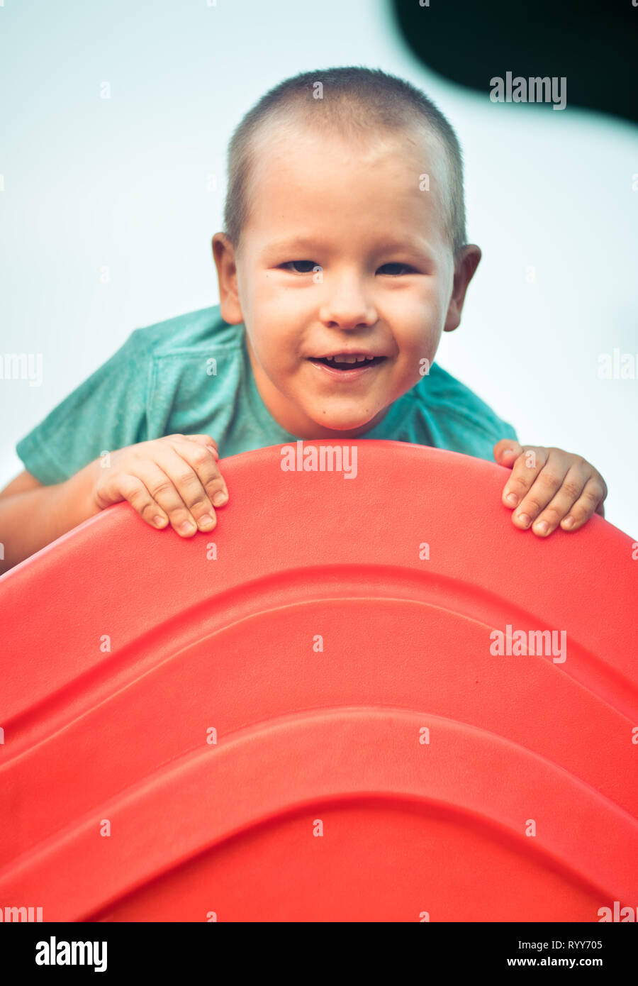 Wenig lächelnde Junge spielt auf einer Folie. Aktivitäten im Freien Stockfoto