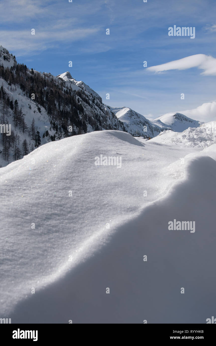 Eine schöne Winterlandschaft mit schneebedeckten Bergen und blauen Himmel im Hintergrund, und mit einem hohen Schnee auf der Piste im Vordergrund; sonnig da Stockfoto