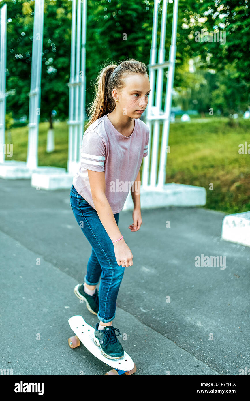 Ein Mädchen ist eine Schülerin von 12-15 Jahre alt, reiten ein Skateboard  im Sommer in der Stadt, eine asphaltierte Straße. Legere Kleidung, Jeans  Turnschuhe T-Shirt Stockfotografie - Alamy