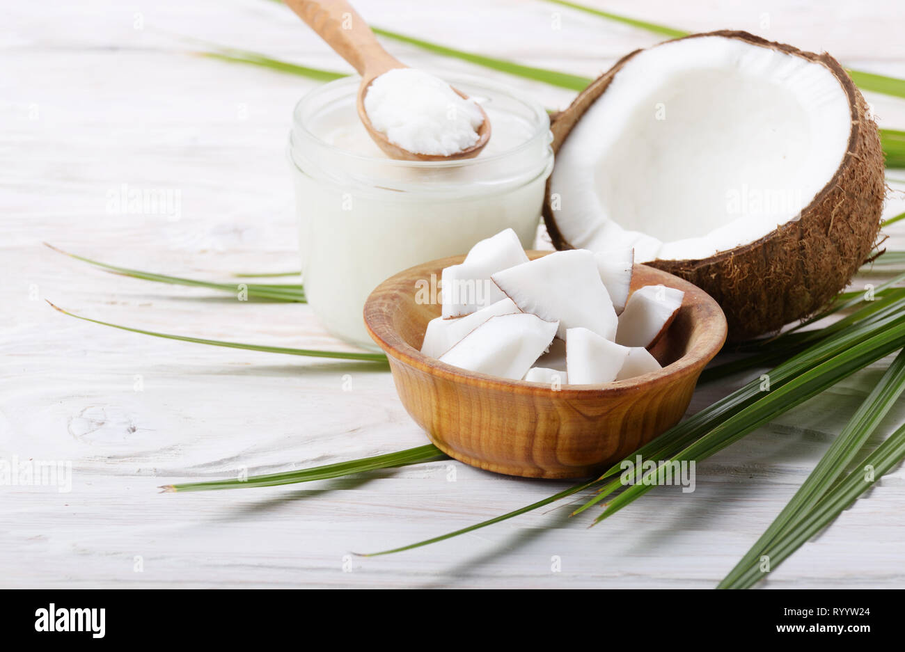 Coconut shell Schwer öl in Glas und Kokosnuss Fleischstücke in Schüssel auf weiße Holztisch Stockfoto