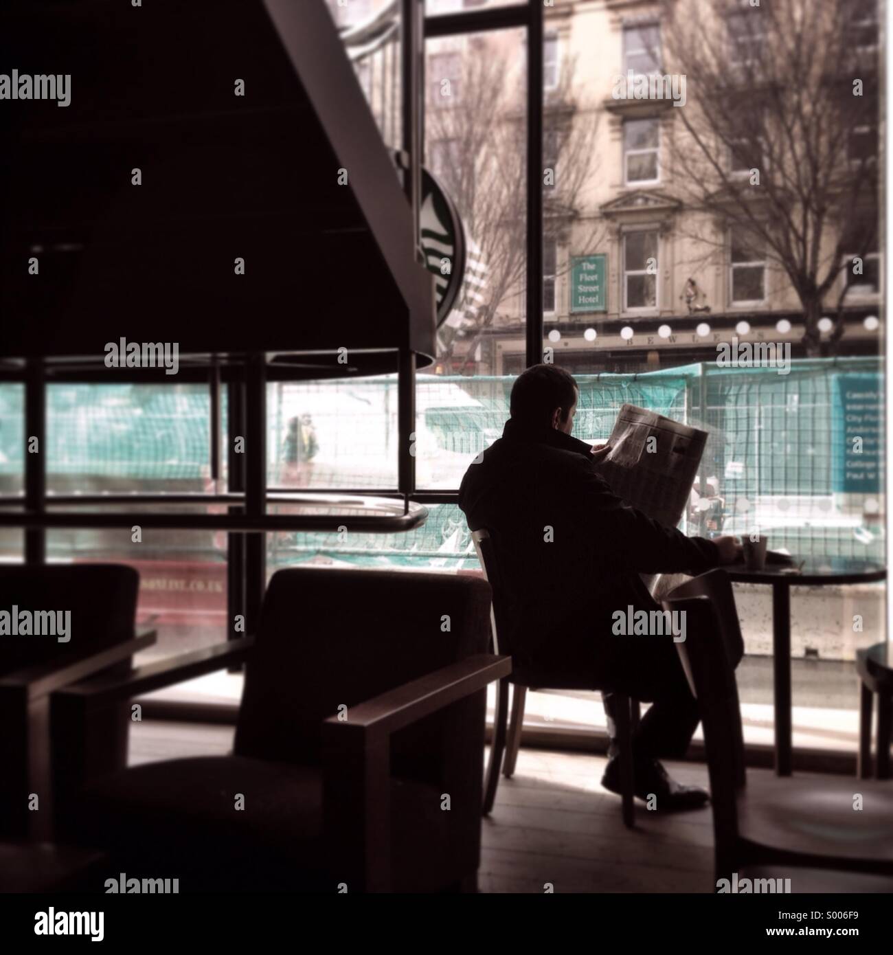 Ein Starbucks-Kunden liest seine Zeitung in einer ruhigen Café. Stockfoto