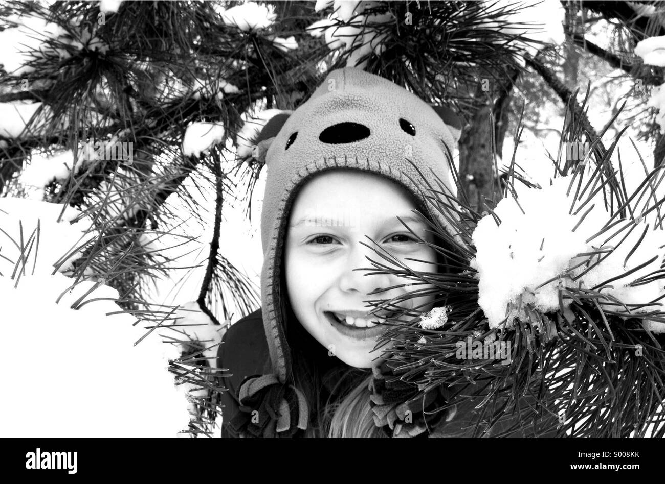 Spielen ist den frisch gefallenen Schnee, eine Mädchen späht heraus unter einem Baum. Stockfoto