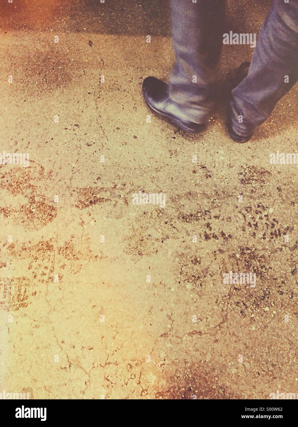 Beine und Füße eines Mannes in Schwarz Schuhe und casual Lshirt stehend auf einem Zementuntergrund mit nassen Fußspuren vorbei. Stockfoto