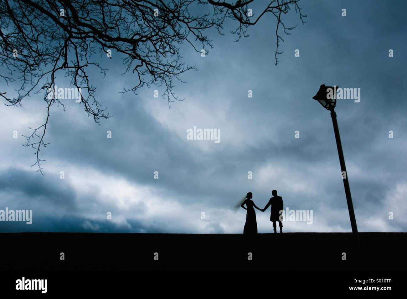 Braut und Bräutigam Hand in Hand neben dem Baum und dem Laternenpfahl Silhouette Stockfoto
