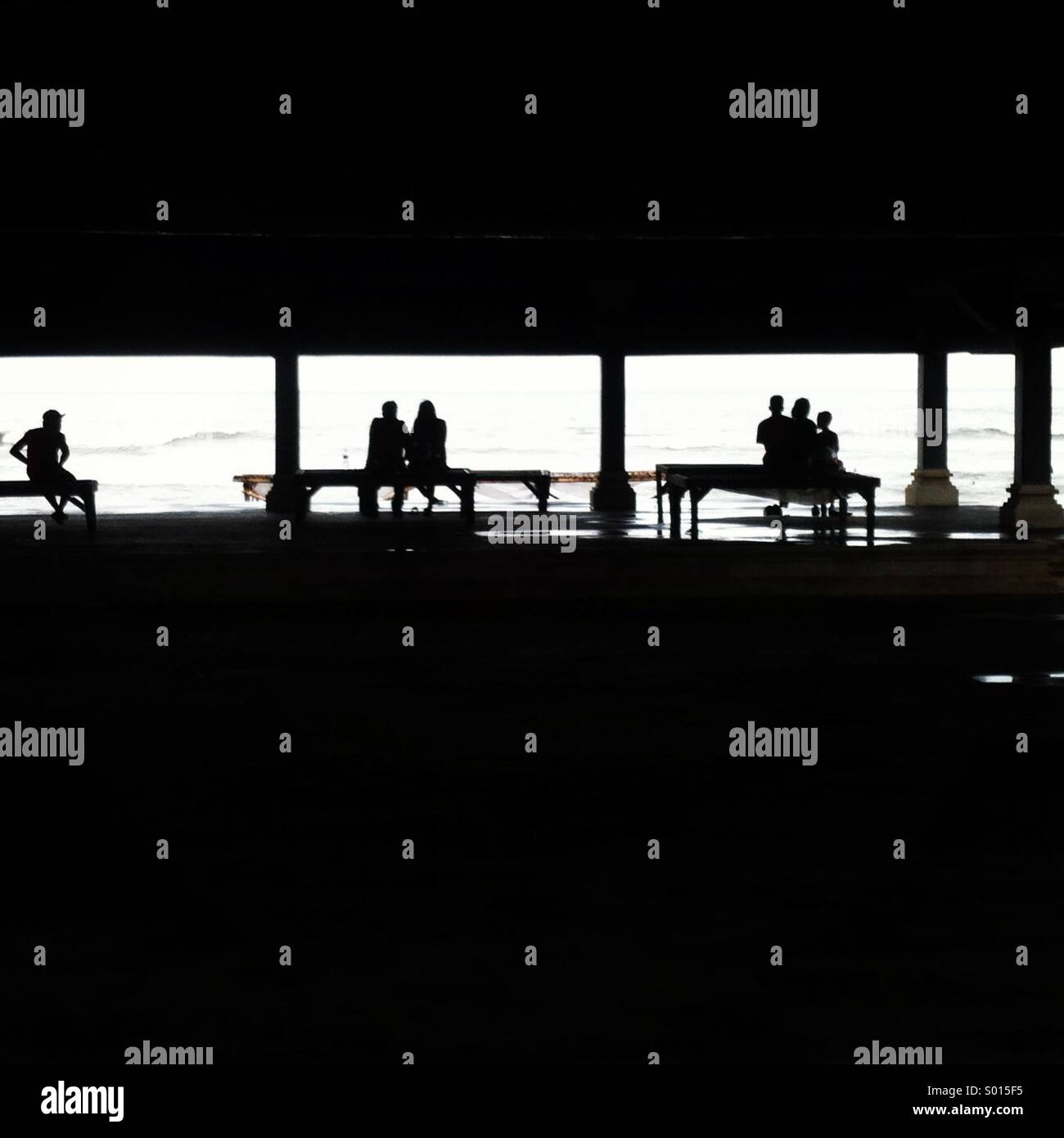 Schwarz / weiß Bild der Silhouette des Menschen sitzen auf drei Bänke mit Blick auf das Meer, Rücken gerichteten Kamera und Rahmen von schwarzen Negativraum... Stockfoto