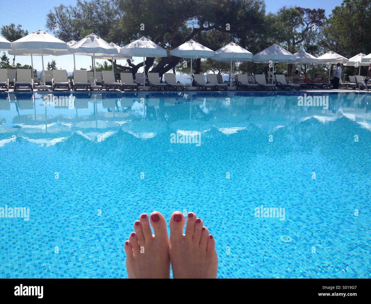 Füße einer Frau Sonnenbaden auf einen leeren Pool in einem türkischen Urlaubsort Stockfoto