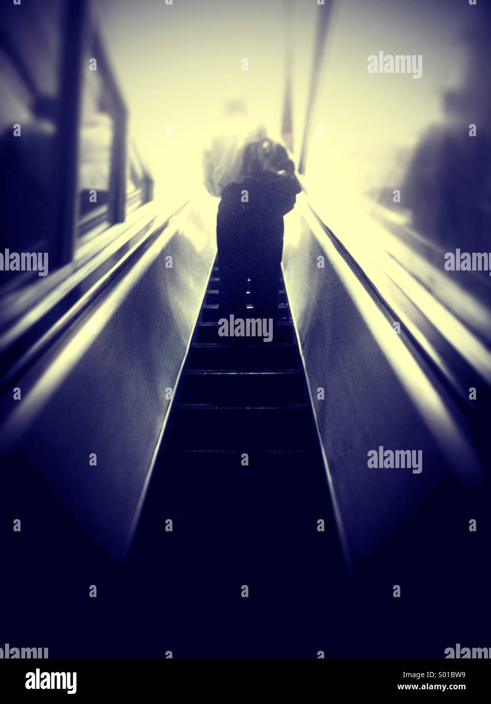 Als Business-Mann eine Rolltreppe hinauf in ein geheimnisvolles weißes Licht reitet Stockfoto