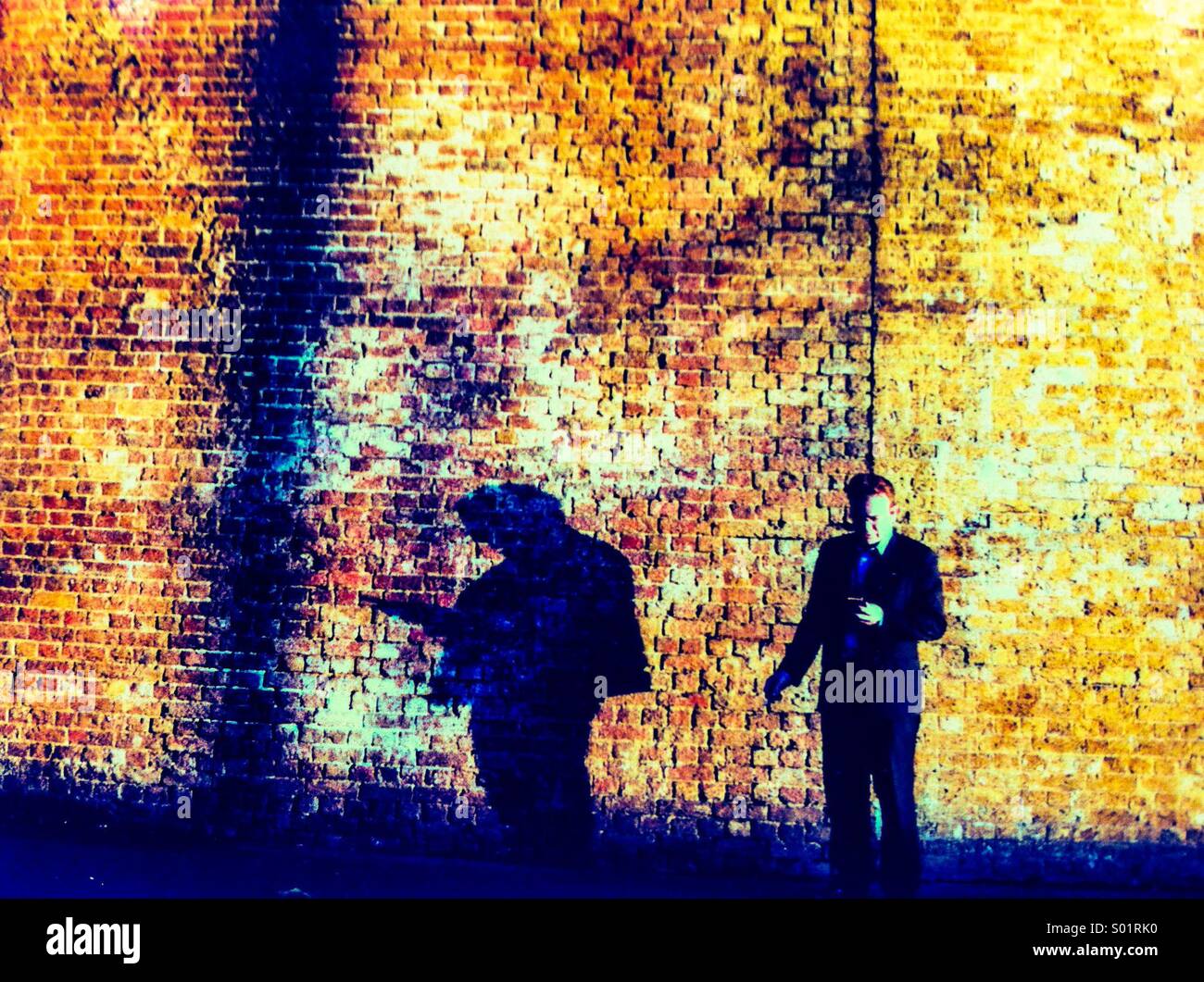 Mann mit mobilen mit seinem Schatten an Wand Stockfoto