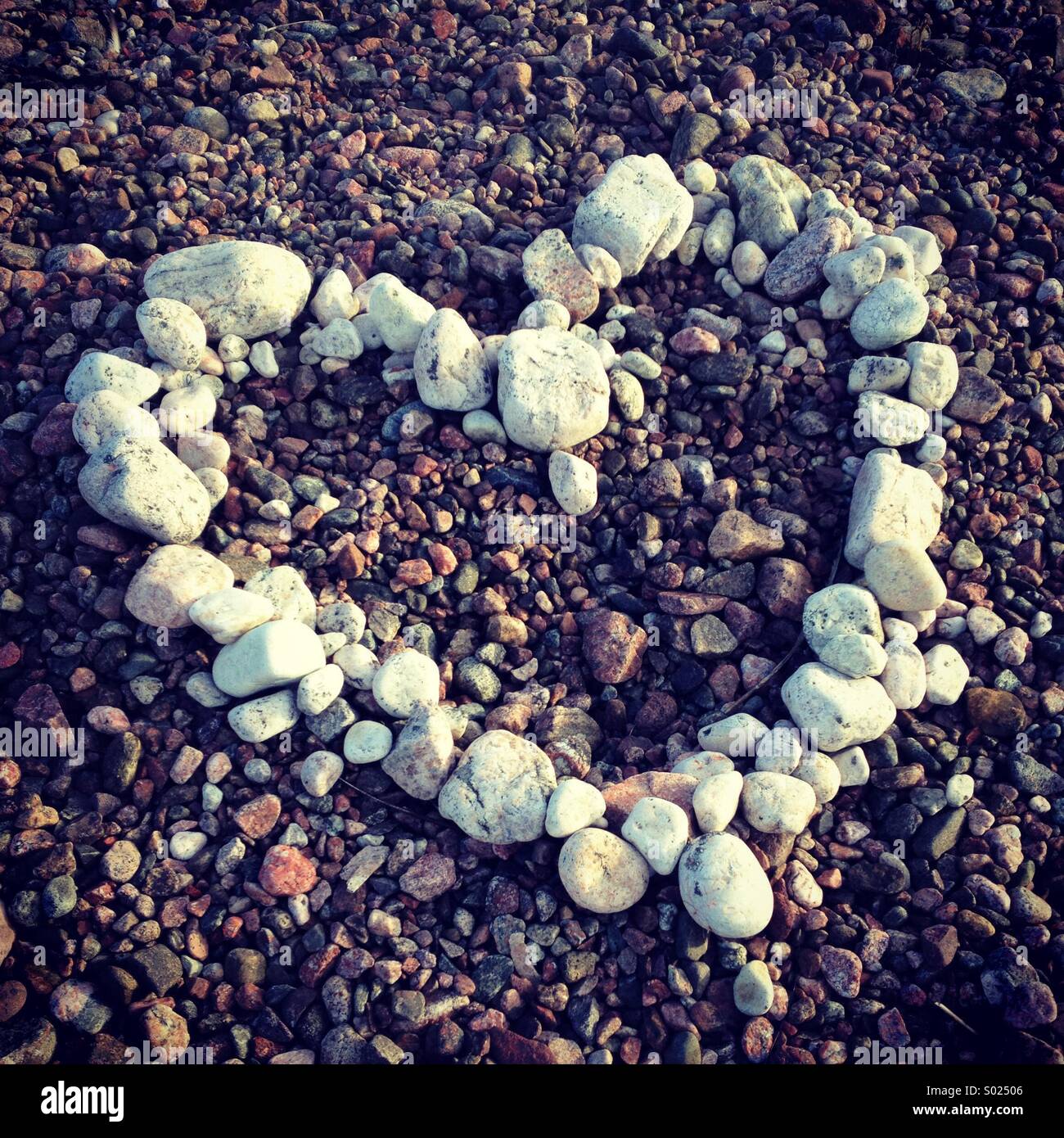 Ein Herz mit weißen Steinen und Kieseln an einem bunten Strand gemacht Stockfoto