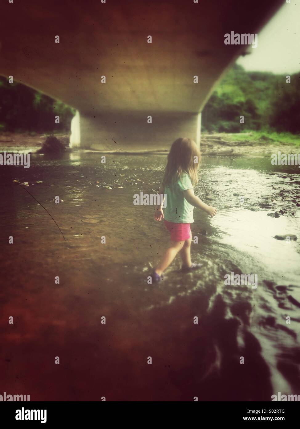 Mädchen in einem Fluss unter der Brücke zu Fuß Stockfoto
