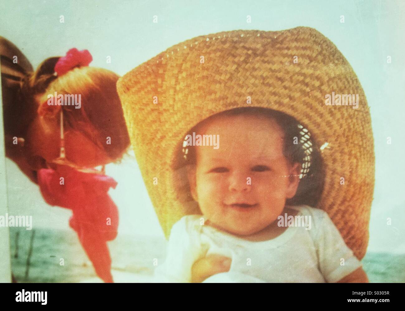 Baby im Alter von 3-6 Monaten mit Strohhut am Strand Stockfoto