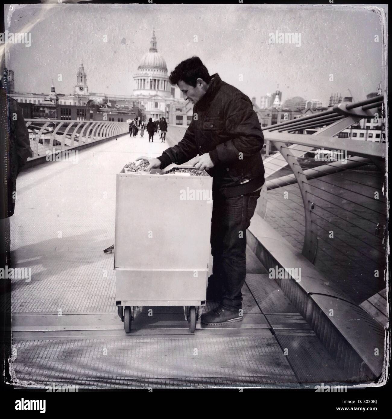 Schwarz / weiß Foto des Verkaeufers Streetfood Verkauf kandierten Nüssen aus seinem Stall auf Millennium Bridge, London, im Schatten der St. Pauls Cathedral. Stockfoto