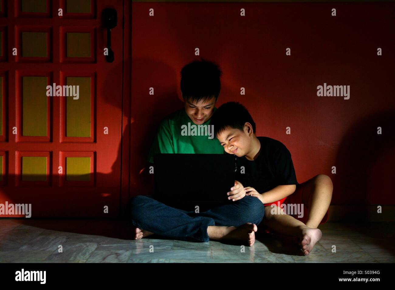 Junge asiatische Kinder oder Geschwister mit einem Laptop-Computer in einem leeren Wohnzimmer Stockfoto