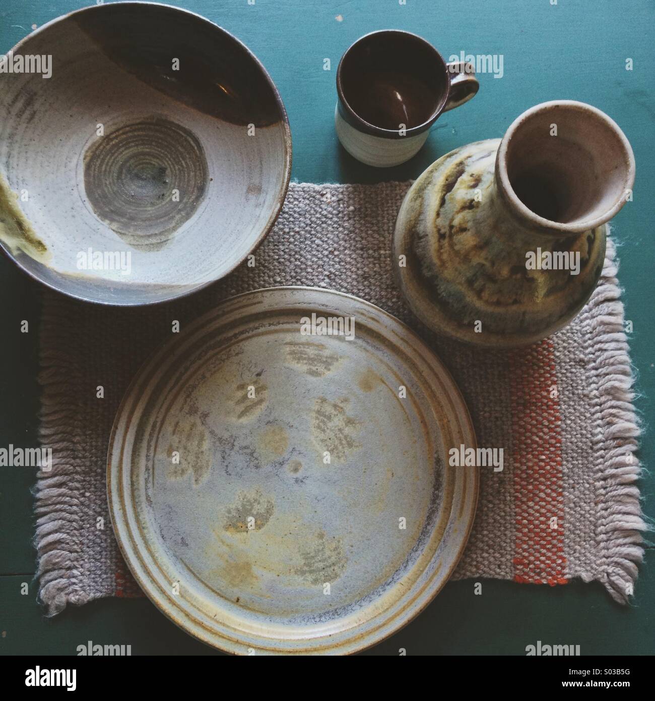 Verschiedene handgemachte Keramik-Keramik am grünen Tisch mit Retro-Wolle Tischset und natürliches Licht Stockfoto