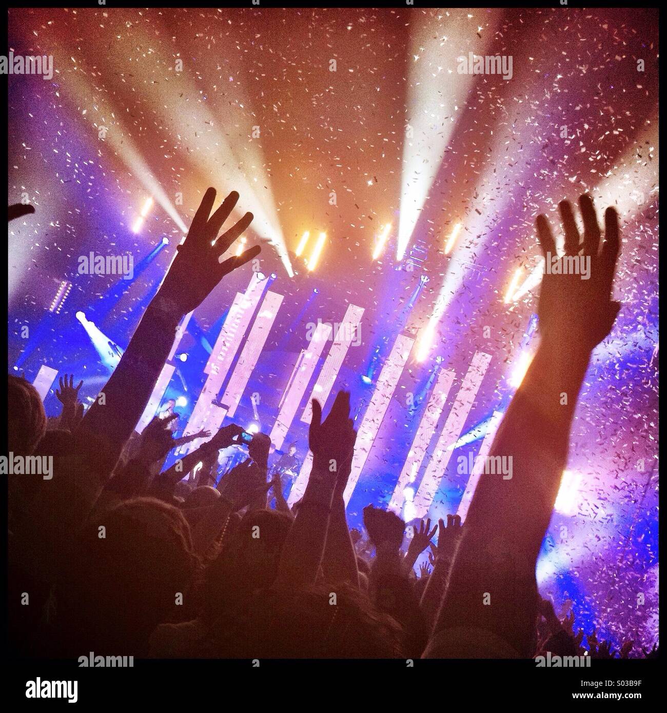 Publikum ein Konzert werfen die Hände in die Luft vor der Bühnenbeleuchtung und Konfetti. Stockfoto